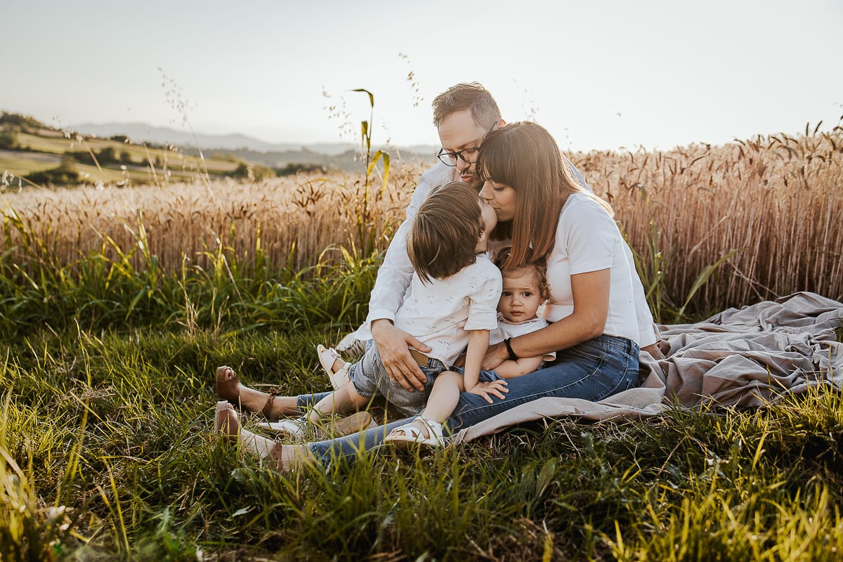 Foto di Famiglia al Tramonto: Ilenia, Filippo, Edoardo e Camilla a Mombello di Torino. la famiglia seduta in un sentiero tra due campi di grano.Il tenero gesto di un bambino che dimostra il suo amore per la mamma