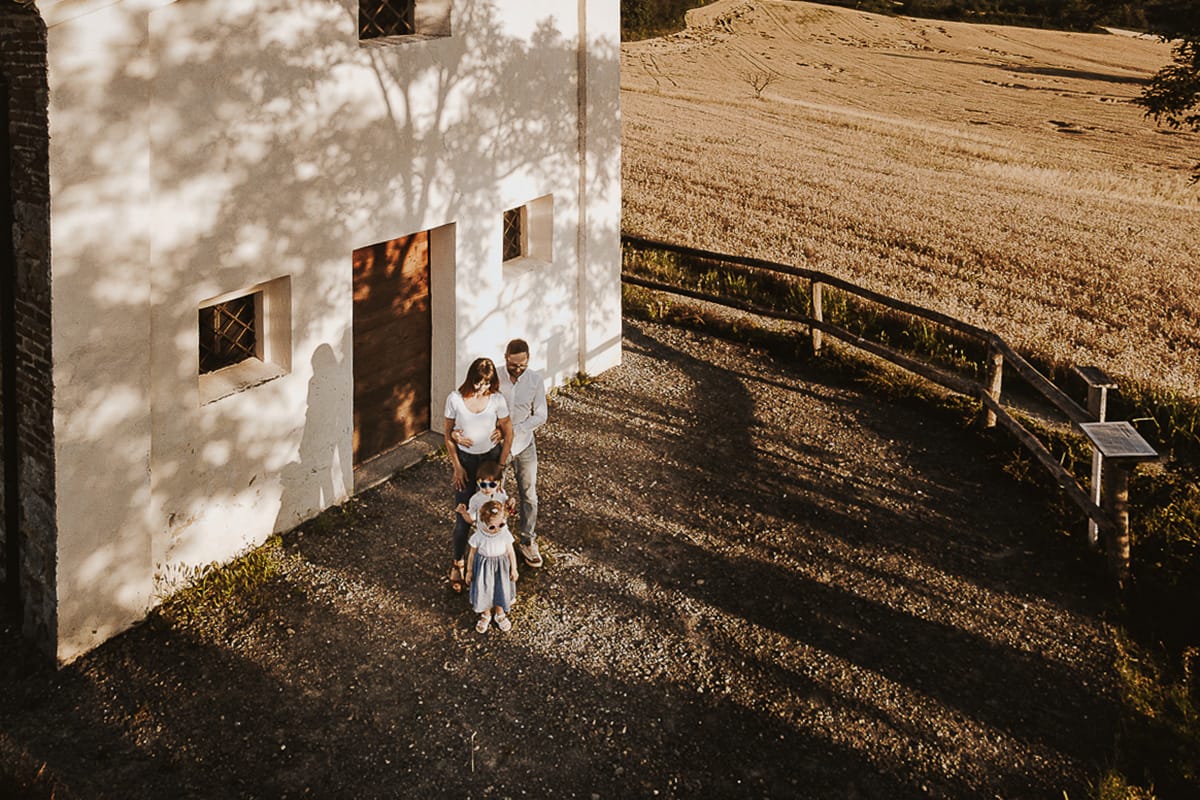 Ilenia e Filippo si stringono in un abbraccio d'amore, mentre i loro figli giocano felici al tramonto.