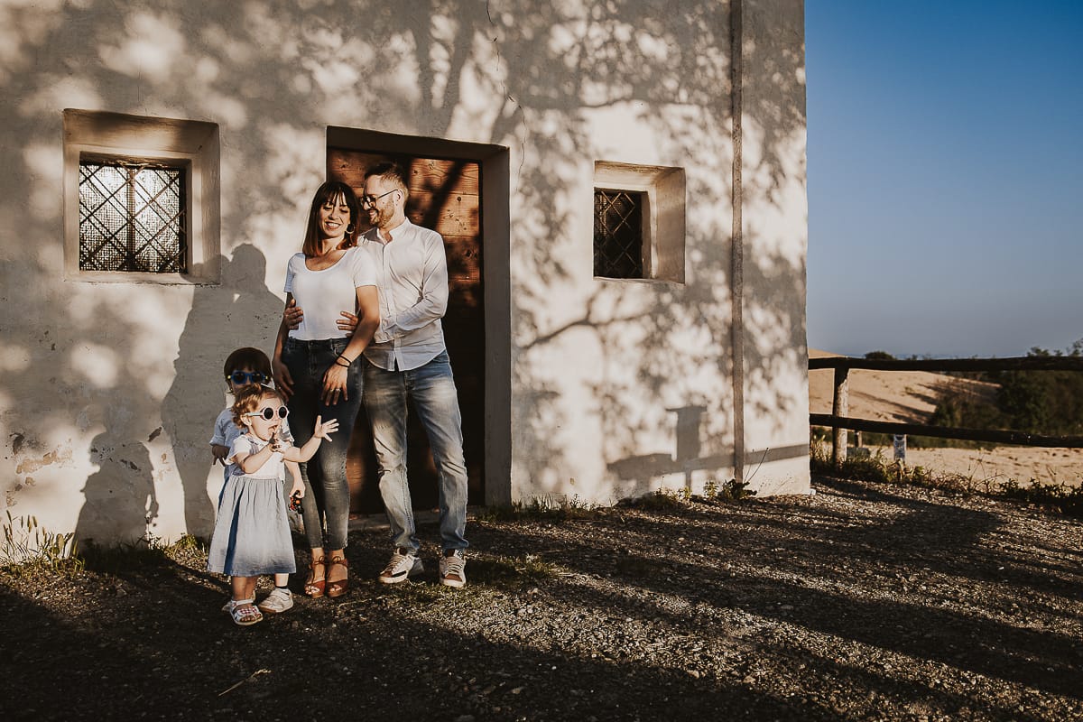 Ilenia e Filippo si stringono in un abbraccio d'amore, mentre i loro figli giocano felici al tramonto.