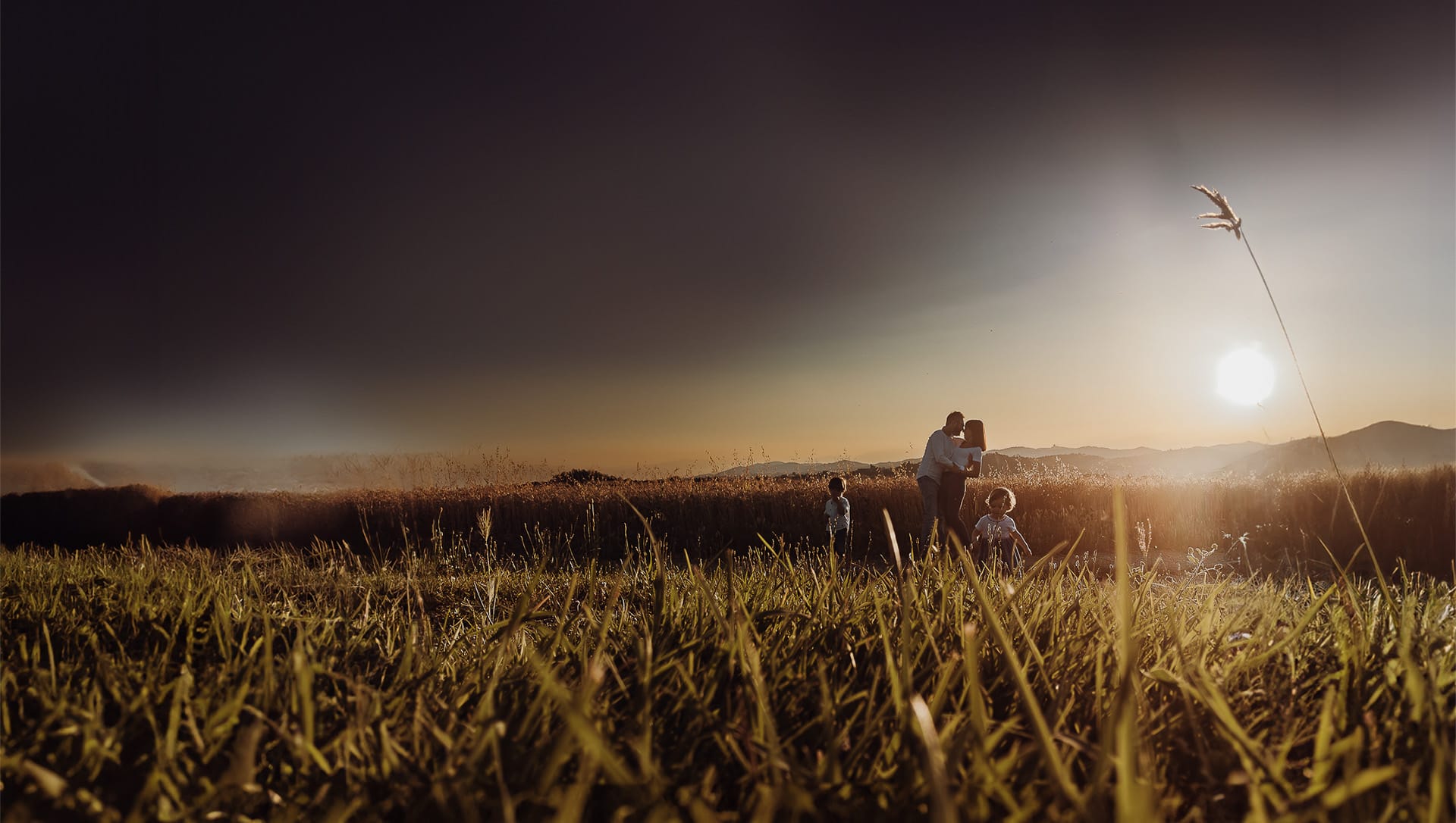 Foto di Famiglia al Tramonto. La magia di un abbraccio di mamma e papà sotto lo sguardo dei due bambini. Controluce. Silhouette.