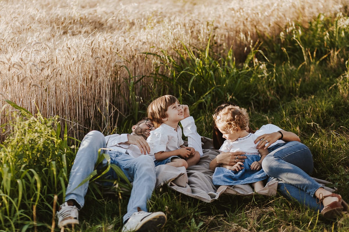 Foto di Famiglia al Tramonto: Ilenia, Filippo, Edoardo e Camilla a Mombello di Torino. la famiglia sdraiata nel sentiero in mezzo a due campi di grano. I bambini sono incuriositi dal drone.