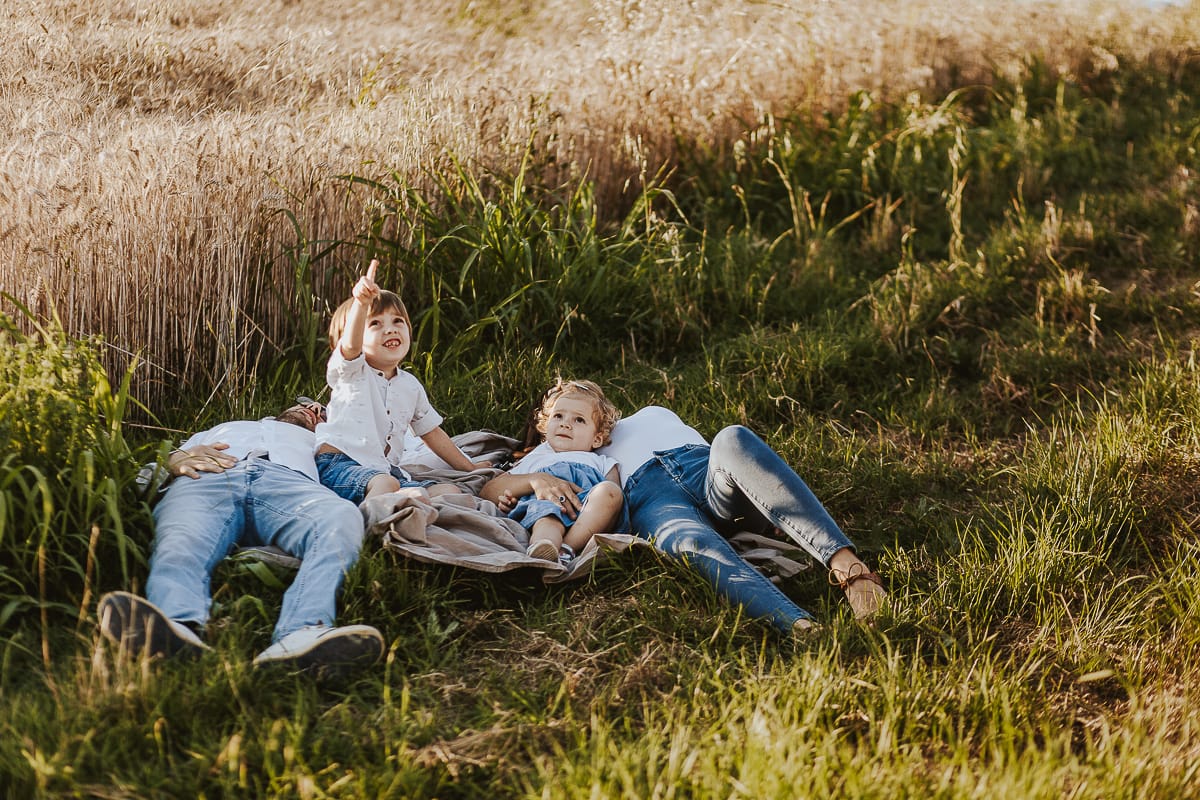 Foto di Famiglia al Tramonto: Ilenia, Filippo, Edoardo e Camilla a Mombello di Torino. la famiglia sdraiata nel sentiero in mezzo a due campi di grano. I bambini sono incuriositi dal drone.