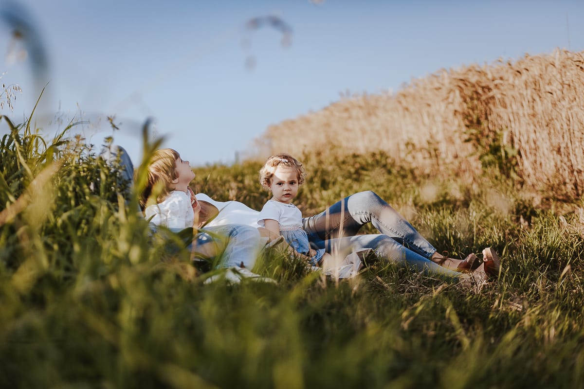 Foto di Famiglia al Tramonto: Ilenia, Filippo, Edoardo e Camilla a Mombello di Torino. la famiglia sdraiata nel sentiero in mezzo a due campi di grano. I bambini sono incuriositi dal drone.