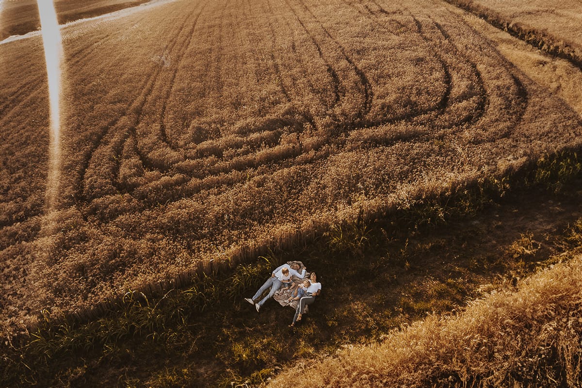 Foto di Famiglia al Tramonto: Ilenia, Filippo, Edoardo e Camilla a Mombello di Torino. la famiglia sdraiata nel sentiero in mezzo a due campi di grano. I bambini sono incuriositi dal drone. Foto dal drone.