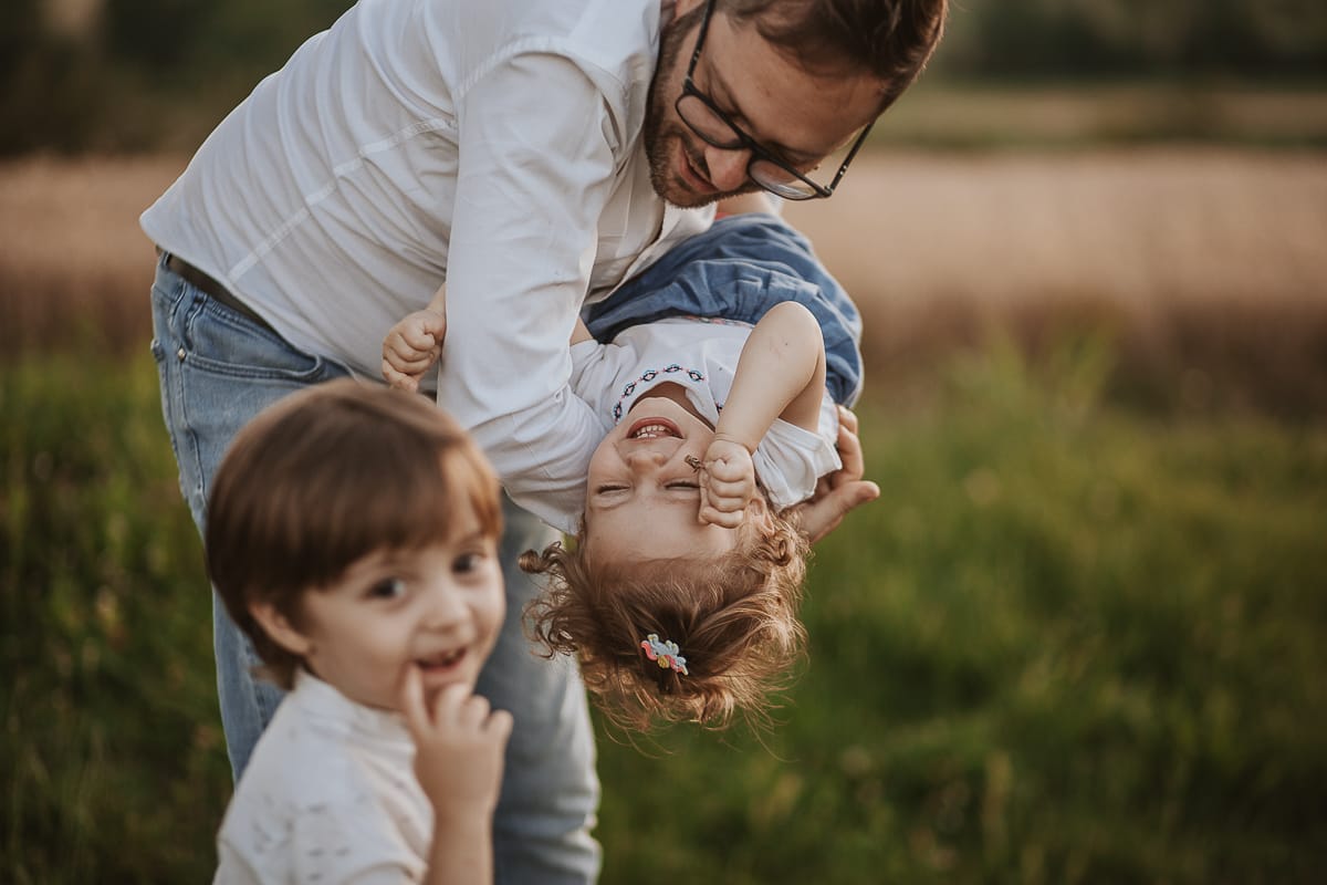 Fotografia di famiglia al tramonto. Il papà gioca con i figli.
