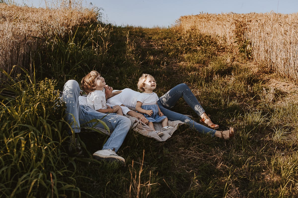Foto di Famiglia al Tramonto: Ilenia, Filippo, Edoardo e Camilla a Mombello di Torino. la famiglia sdraiata nel sentiero in mezzo a due campi di grano. I bambini sono incuriositi dal drone.