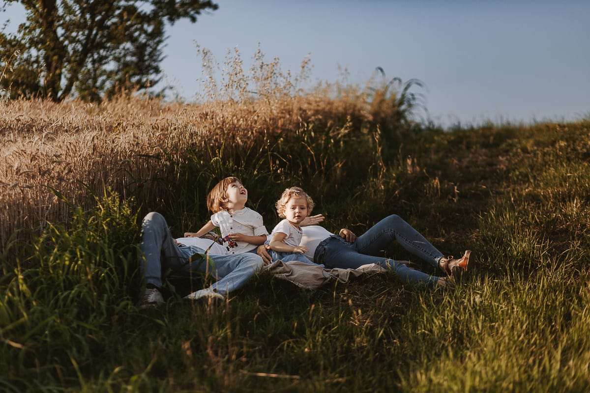 Foto di Famiglia al Tramonto: Ilenia, Filippo, Edoardo e Camilla a Mombello di Torino. la famiglia sdraiata nel sentiero in mezzo a due campi di grano. I bambini sono incuriositi dal drone.