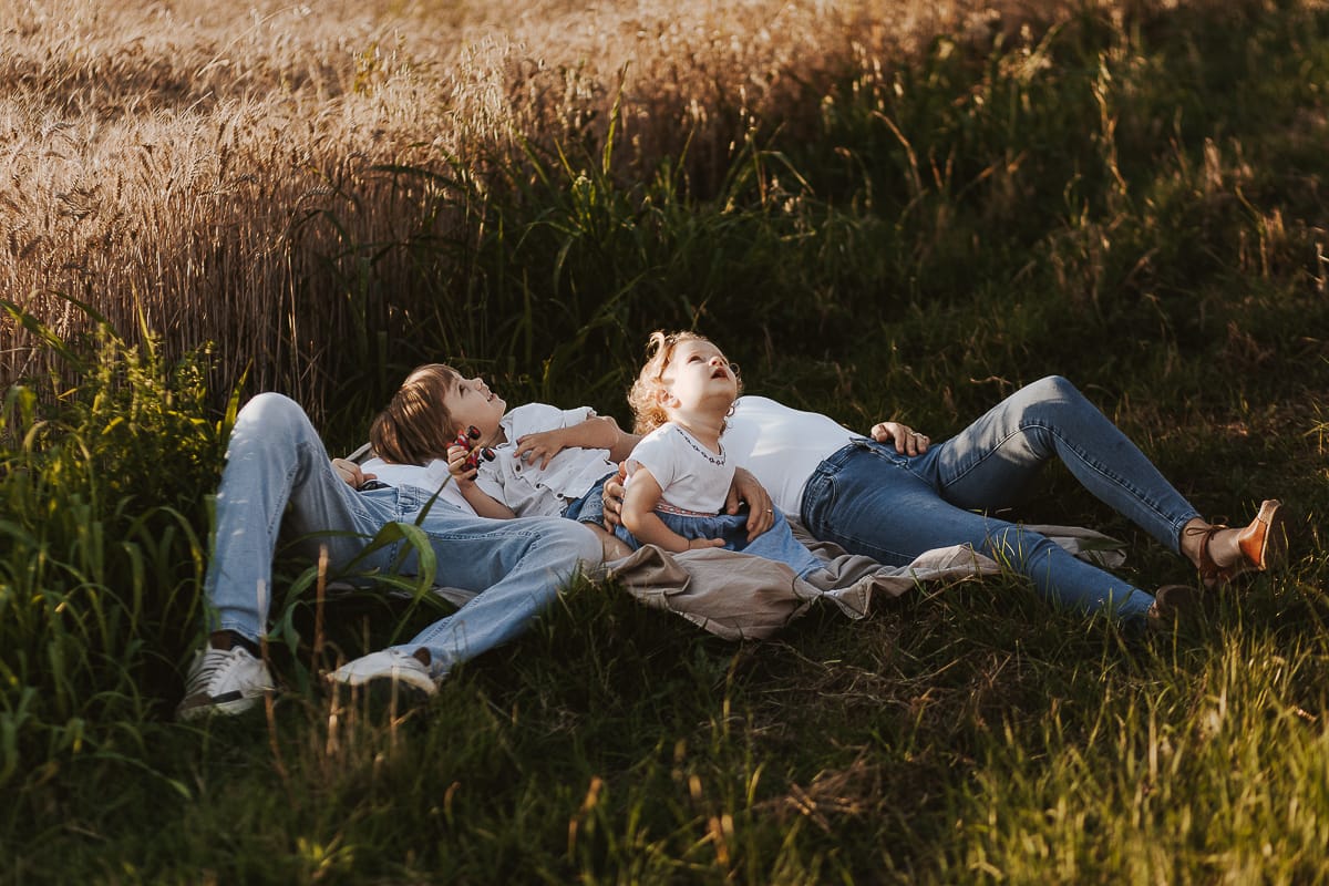 Foto di Famiglia al Tramonto: Ilenia, Filippo, Edoardo e Camilla a Mombello di Torino. la famiglia sdraiata nel sentiero in mezzo a due campi di grano. I bambini sono incuriositi dal drone.