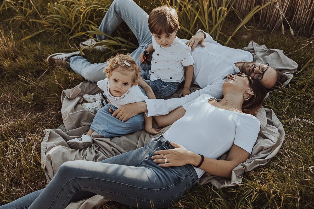 Foto di Famiglia al Tramonto: Ilenia, Filippo, Edoardo e Camilla a Mombello di Torino. la famiglia sdraiata nel sentiero in mezzo a due campi di grano. I bambini sono incuriositi dal drone.