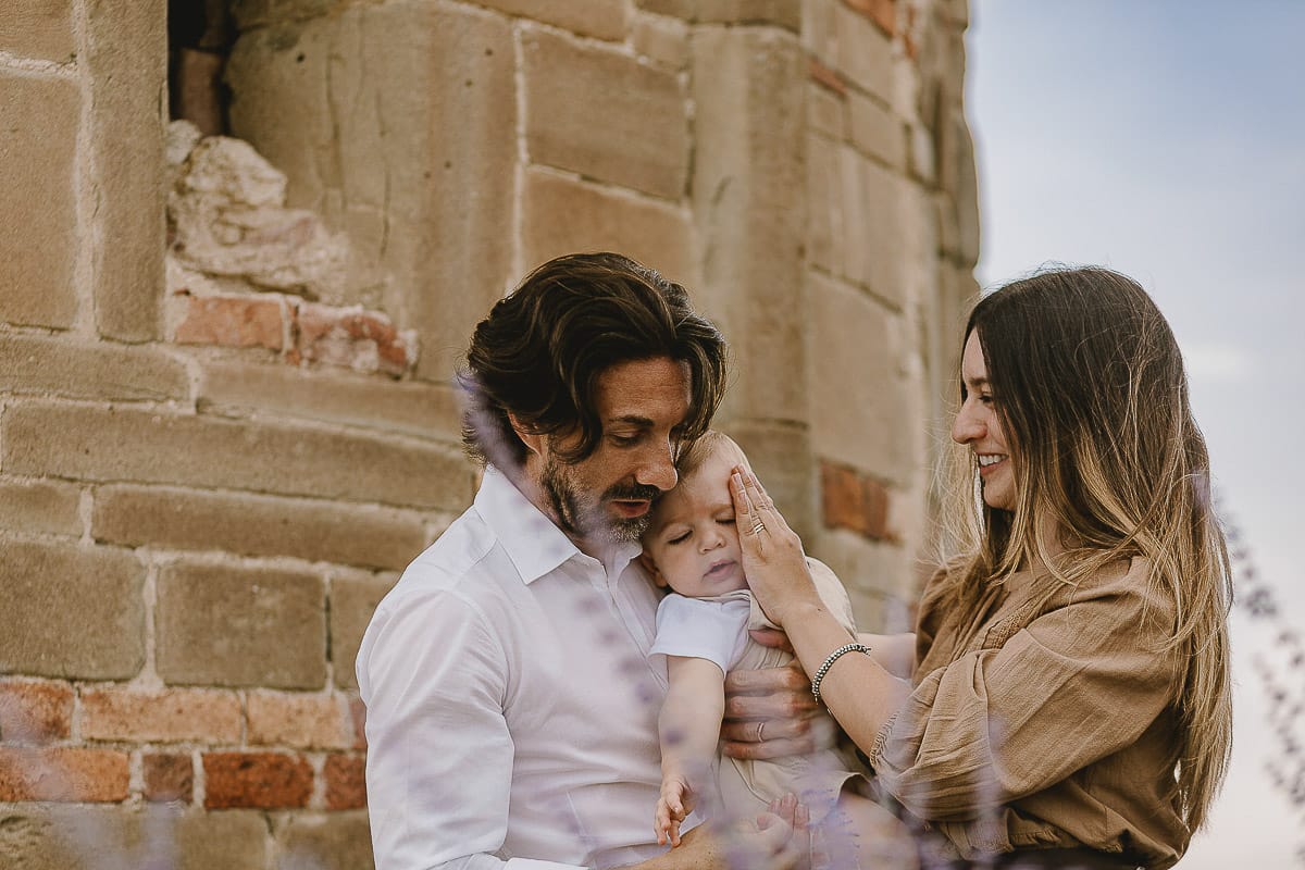 Servizio fotografico di famiglia a Torino: un tramonto dorato a Mombello di Torino. Chiara, Alessandro e leonardo in mezzo ad un cespuglio di fiori di colore lilla davanti alla chiesa romanica di San Lorenzo