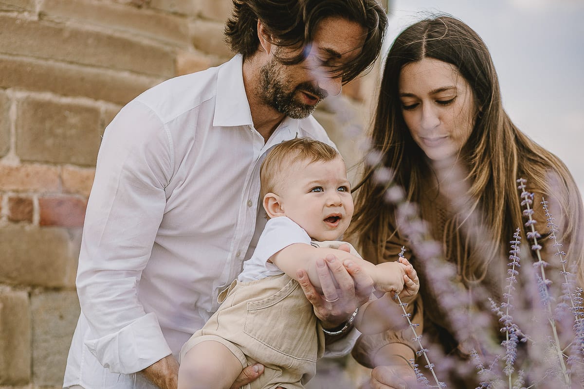 Servizio fotografico di famiglia a Torino: un tramonto dorato a Mombello di Torino. Chiara, Alessandro e leonardo in mezzo ad un cespuglio di fiori di colore lilla davanti alla chiesa romanica di San Lorenzo