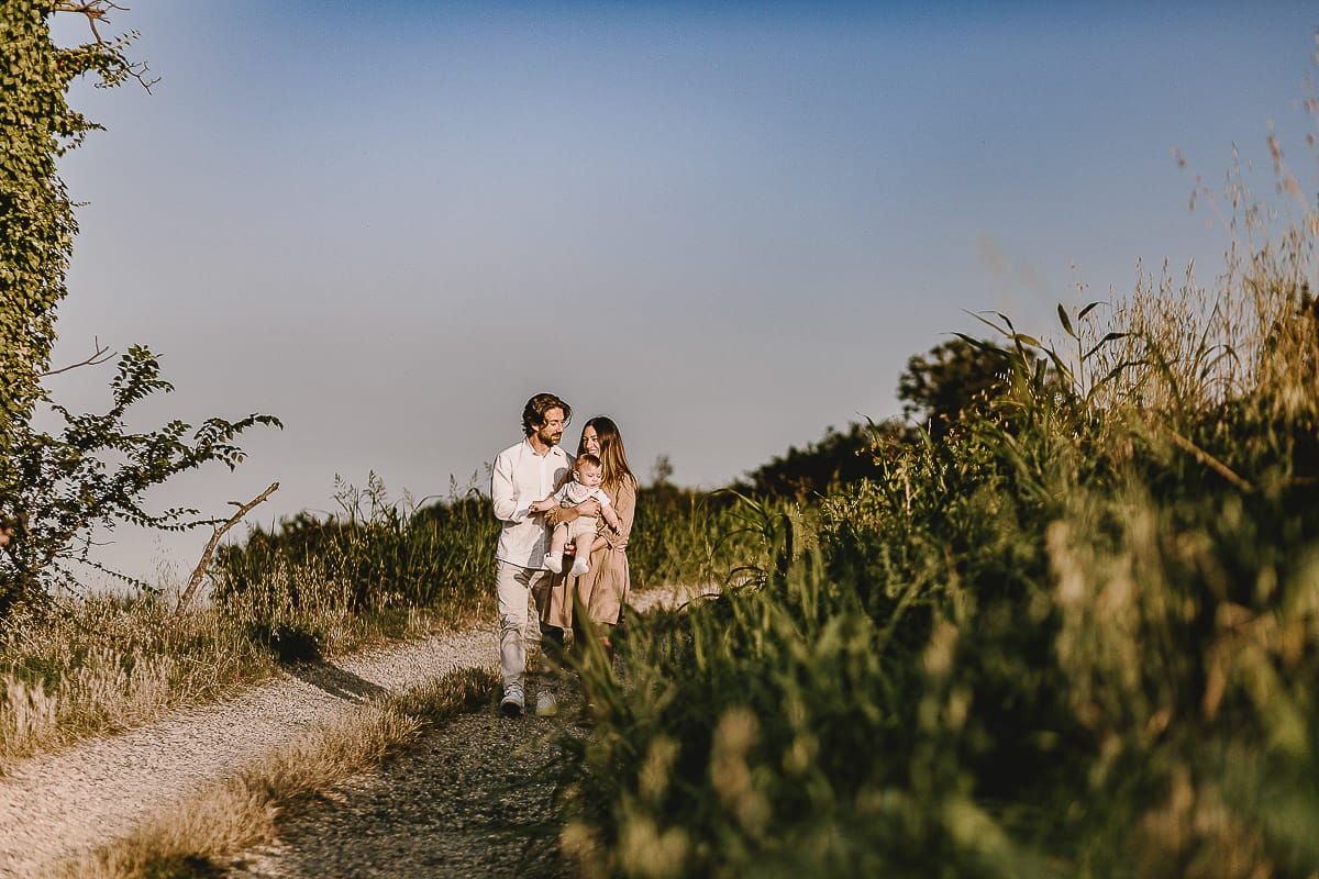 Servizio fotografico di famiglia a Torino: un tramonto dorato a Mombello di Torino. Chiara, Alessandro e il piccolo Leonardo camminano