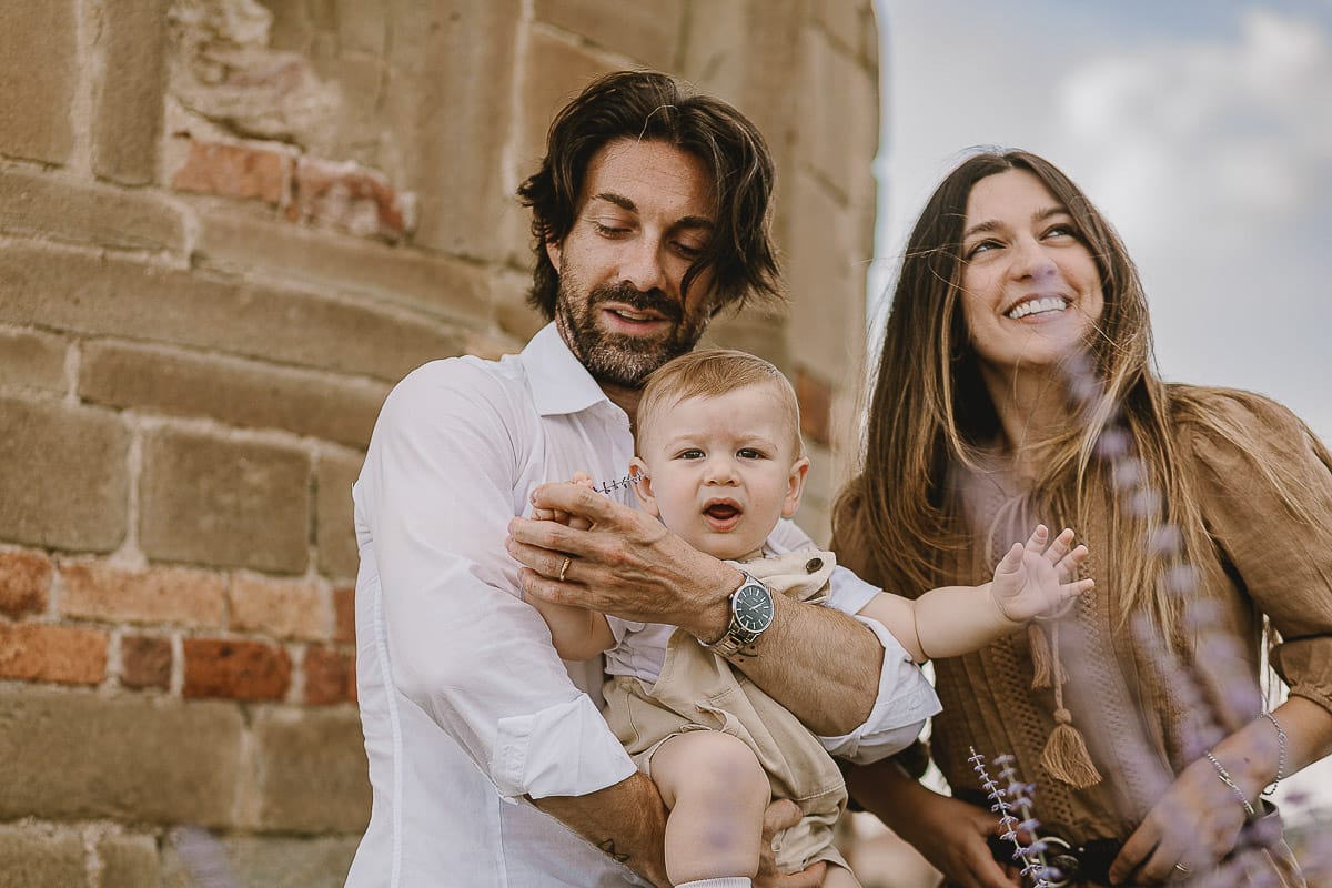 Servizio fotografico di famiglia a Torino: un tramonto dorato a Mombello di Torino. Chiara, Alessandro e leonardo in mezzo ad un cespuglio di fiori di colore lilla davanti alla chiesa romanica di San Lorenzo