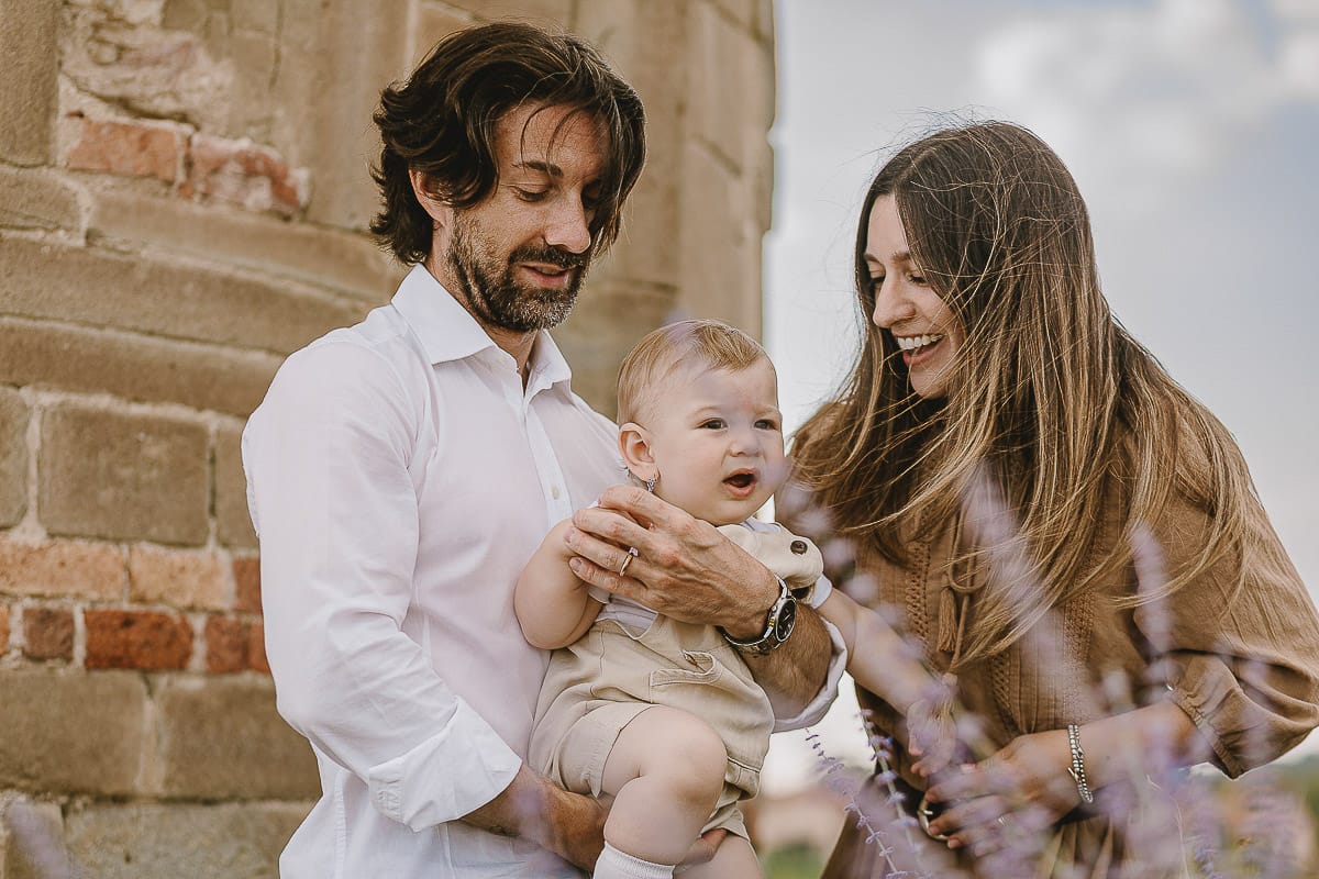 Servizio fotografico di famiglia a Torino: un tramonto dorato a Mombello di Torino. Chiara, Alessandro e leonardo in mezzo ad un cespuglio di fiori di colore lilla davanti alla chiesa romanica di San Lorenzo