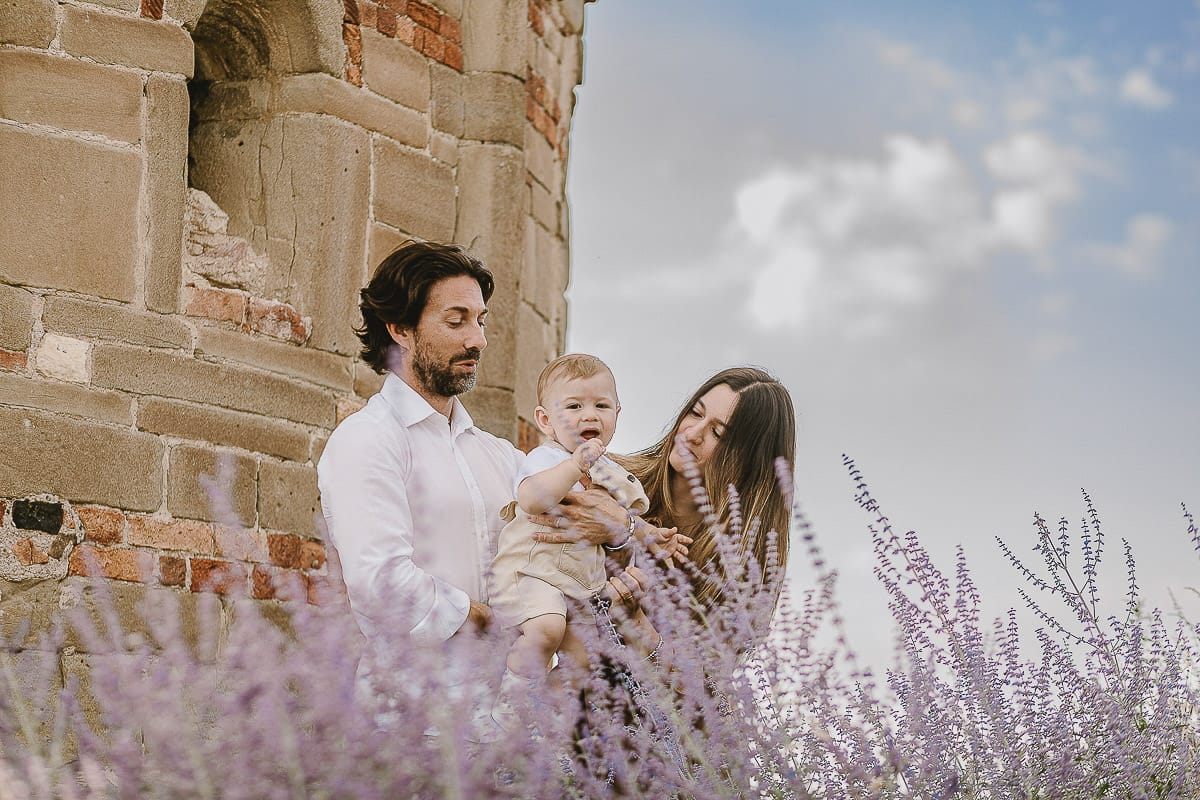 Servizio fotografico di famiglia a Torino: un tramonto dorato a Mombello di Torino. Chiara, Alessandro e leonardo in mezzo ad un cespuglio di fiori di colore lilla davanti alla chiesa romanica di San Lorenzo