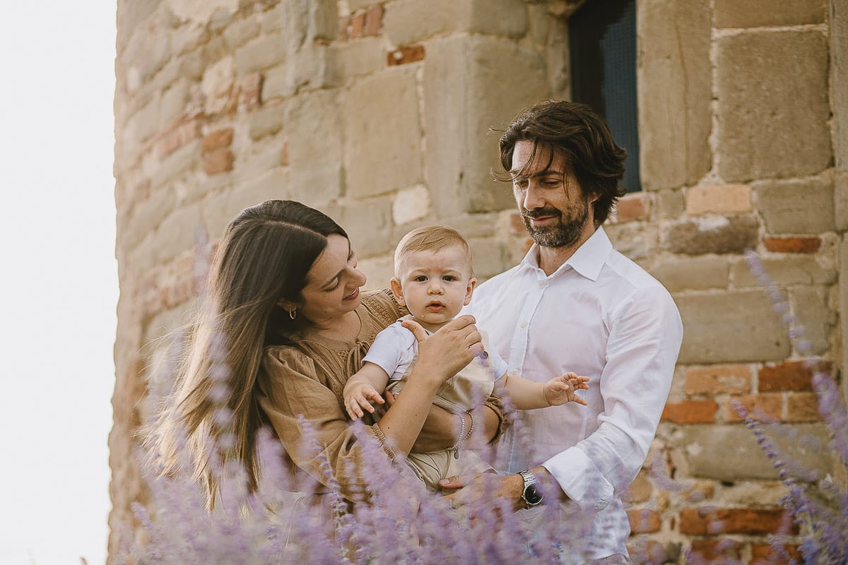 Servizio fotografico di famiglia a Torino: un tramonto dorato a Mombello di Torino. Chiara, Alessandro e leonardo in mezzo ad un cespuglio di fiori di colore lilla davanti alla chiesa romanica di San Lorenzo