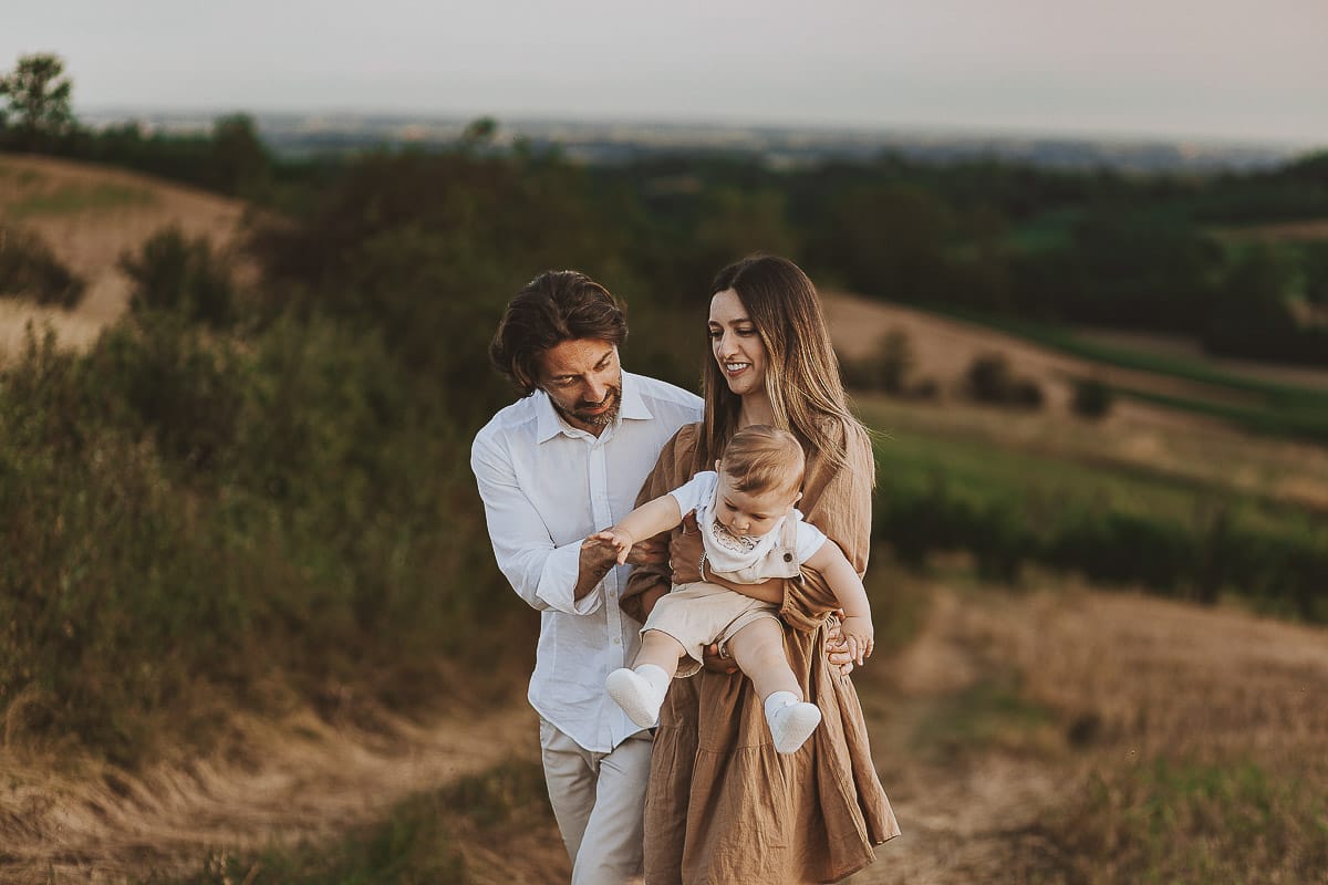 Servizio fotografico di famiglia a Torino: un tramonto dorato a Mombello di Torino. Chiara, Alessandro e il piccolo Leonardo camminano in un campo