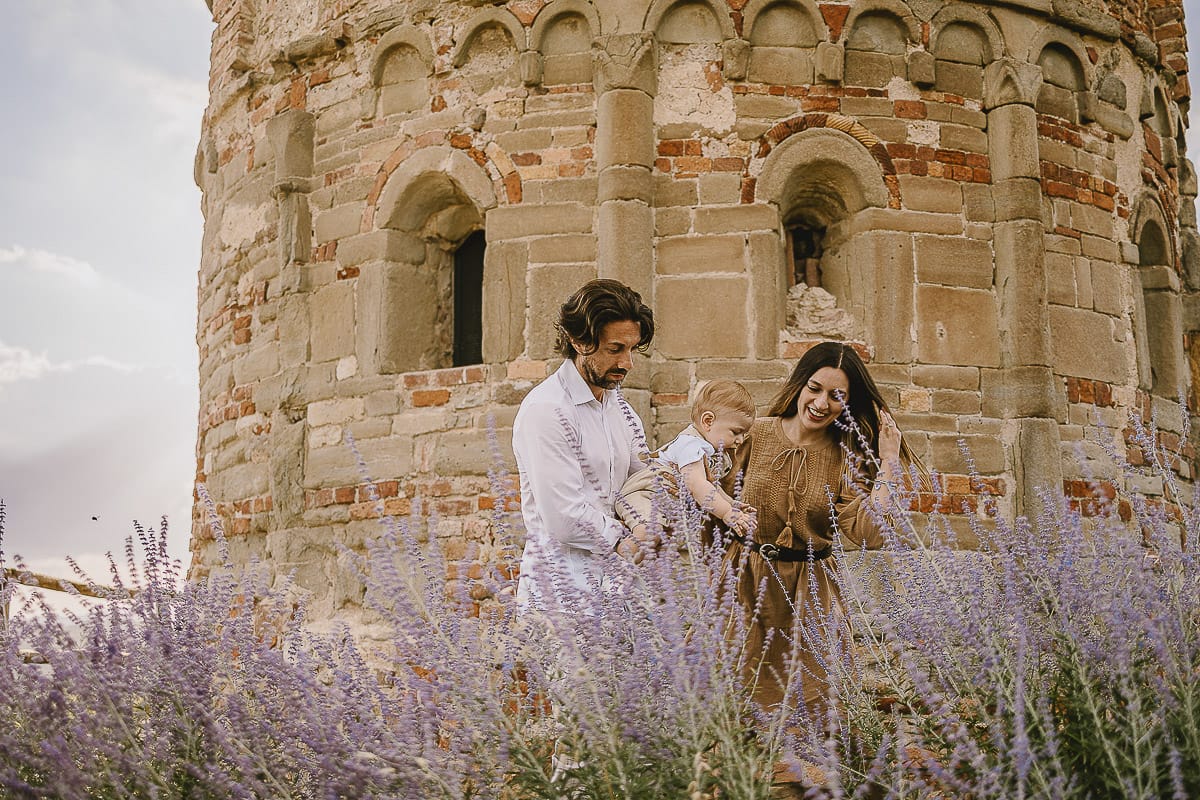 Servizio fotografico di famiglia a Torino: un tramonto dorato a Mombello di Torino. Chiara, Alessandro e leonardo in mezzo ad un cespuglio di fiori di colore lilla davanti alla chiesa romanica di San Lorenzo