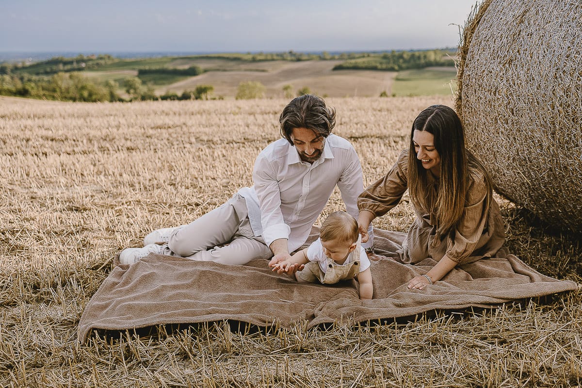 Servizio fotografico di famiglia a Torino: un tramonto dorato a Mombello di Torino. Chiara, Alessandro e il piccolo Leonardo distesi in un campo davanti ad una balla di fieno.