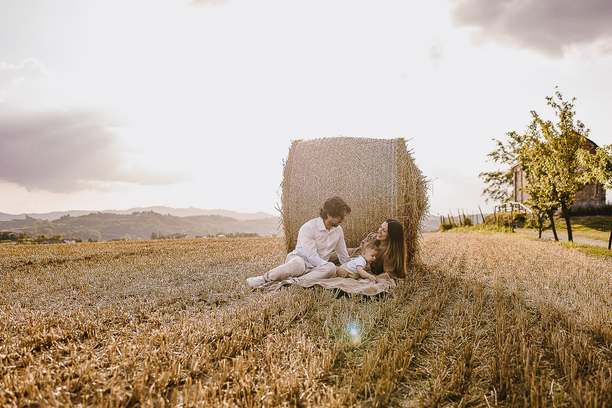 Servizio fotografico di famiglia a Torino: un tramonto dorato a Mombello di Torino. Chiara, Alessandro e il piccolo Leonardo distesi in un campo davanti ad una balla di fieno.