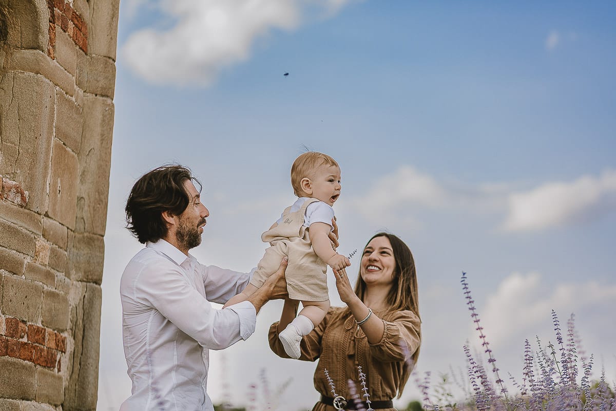 Servizio fotografico di famiglia a Torino: un tramonto dorato a Mombello di Torino. Chiara, Alessandro e leonardo in mezzo ad un cespuglio di fiori di colore lilla davanti alla chiesa romanica di San Lorenzo