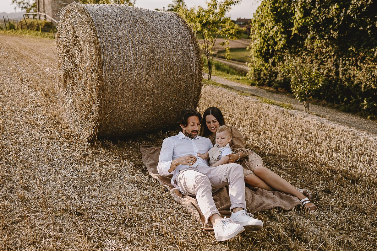 Servizio fotografico di famiglia a Torino: un tramonto dorato a Mombello di Torino. Chiara, Alessandro e il piccolo Leonardo distesi in un campo davanti ad una balla di fieno.