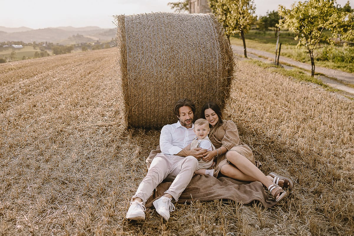 Servizio fotografico di famiglia a Torino: un tramonto dorato a Mombello di Torino. Chiara, Alessandro e il piccolo Leonardo distesi in un campo davanti ad una balla di fieno.