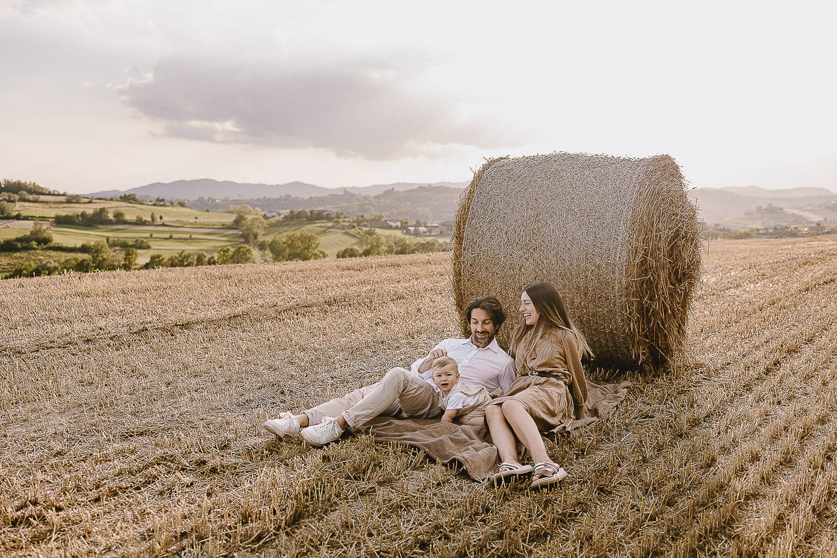 Servizio fotografico di famiglia a Torino: un tramonto dorato a Mombello di Torino. Chiara, Alessandro e il piccolo Leonardo distesi in un campo davanti ad una balla di fieno.