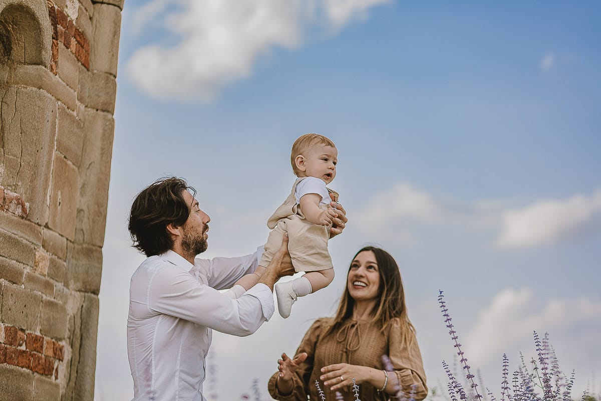 Servizio fotografico di famiglia a Torino: un tramonto dorato a Mombello di Torino. Chiara, Alessandro e leonardo in mezzo ad un cespuglio di fiori di colore lilla davanti alla chiesa romanica di San Lorenzo