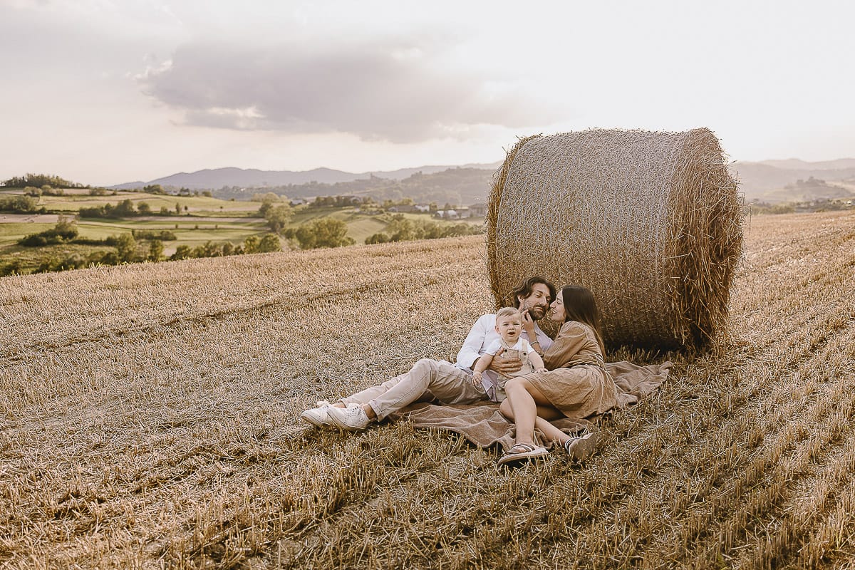 Servizio fotografico di famiglia a Torino: un tramonto dorato a Mombello di Torino. Chiara, Alessandro e il piccolo Leonardo distesi in un campo davanti ad una balla di fieno.
