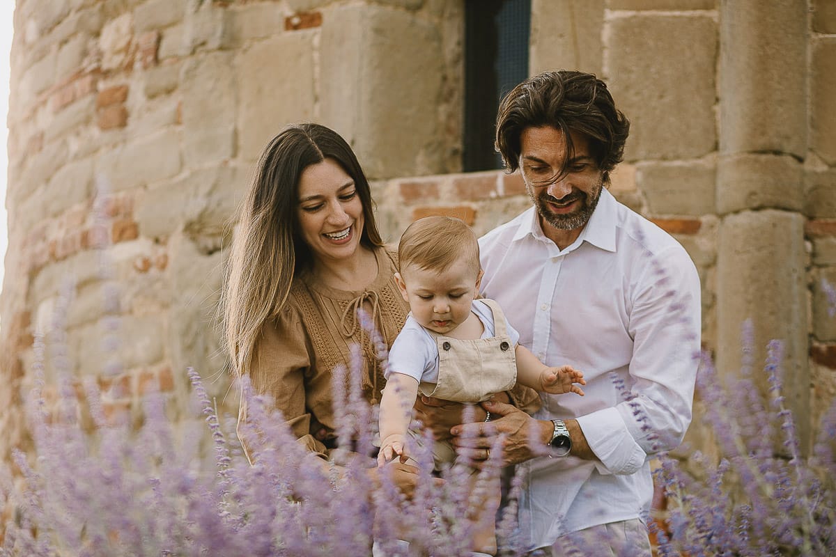 Servizio fotografico di famiglia a Torino: un tramonto dorato a Mombello di Torino. Chiara, Alessandro e leonardo in mezzo ad un cespuglio di fiori di colore lilla davanti alla chiesa romanica di San Lorenzo