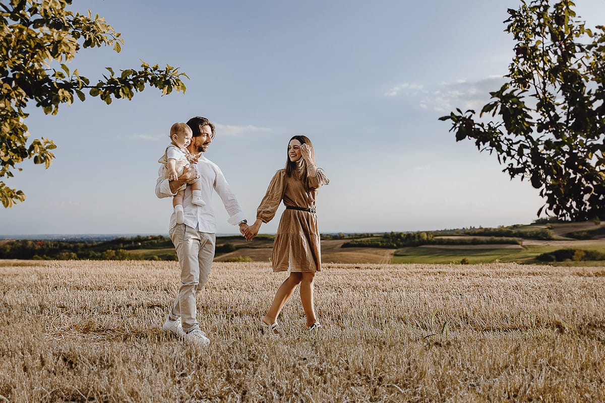 Servizio fotografico di famiglia a Torino: un tramonto dorato a Mombello di Torino. Chiara, Alessandro e il piccolo Leonardo camminano