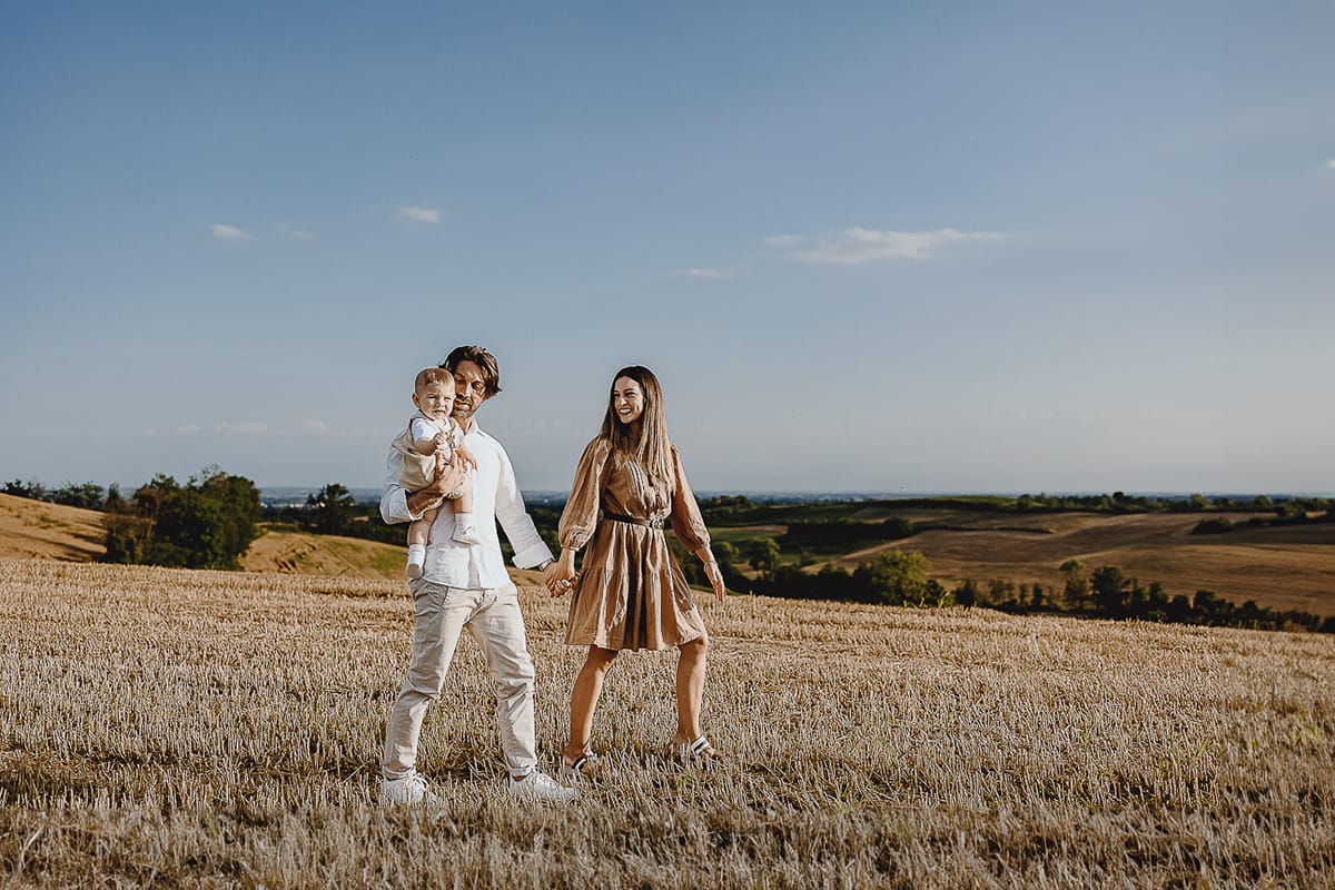 Servizio fotografico di famiglia a Torino: un tramonto dorato a Mombello di Torino. Chiara, Alessandro e il piccolo Leonardo camminano