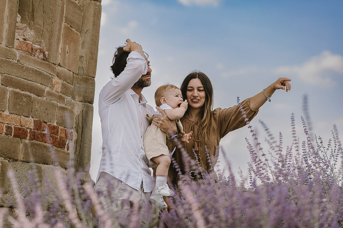 Servizio fotografico di famiglia a Torino: un tramonto dorato a Mombello di Torino. Chiara, Alessandro e leonardo in mezzo ad un cespuglio di fiori di colore lilla davanti alla chiesa romanica di San Lorenzo
