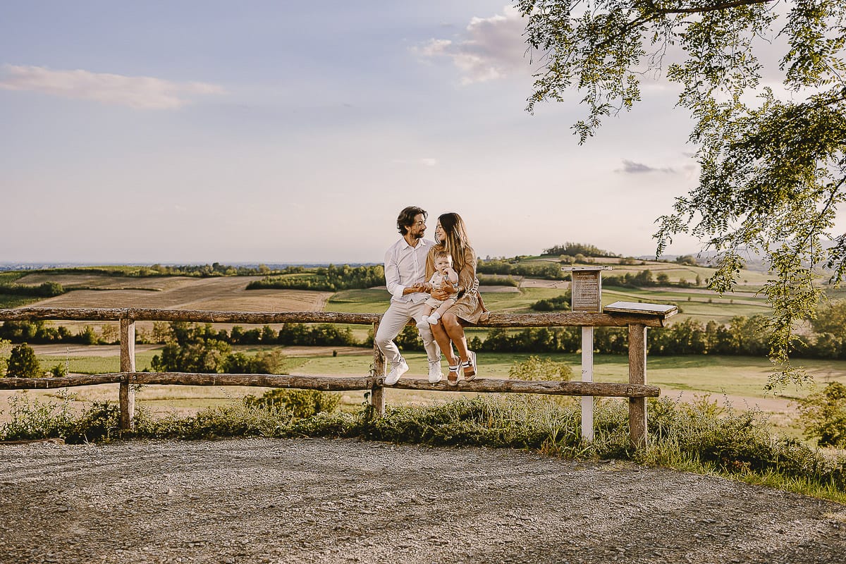 Servizio fotografico di famiglia a Torino: un tramonto dorato a Mombello di Torino. Chiara, Alessandro e il piccolo Leonardo seduti su di una staccionata