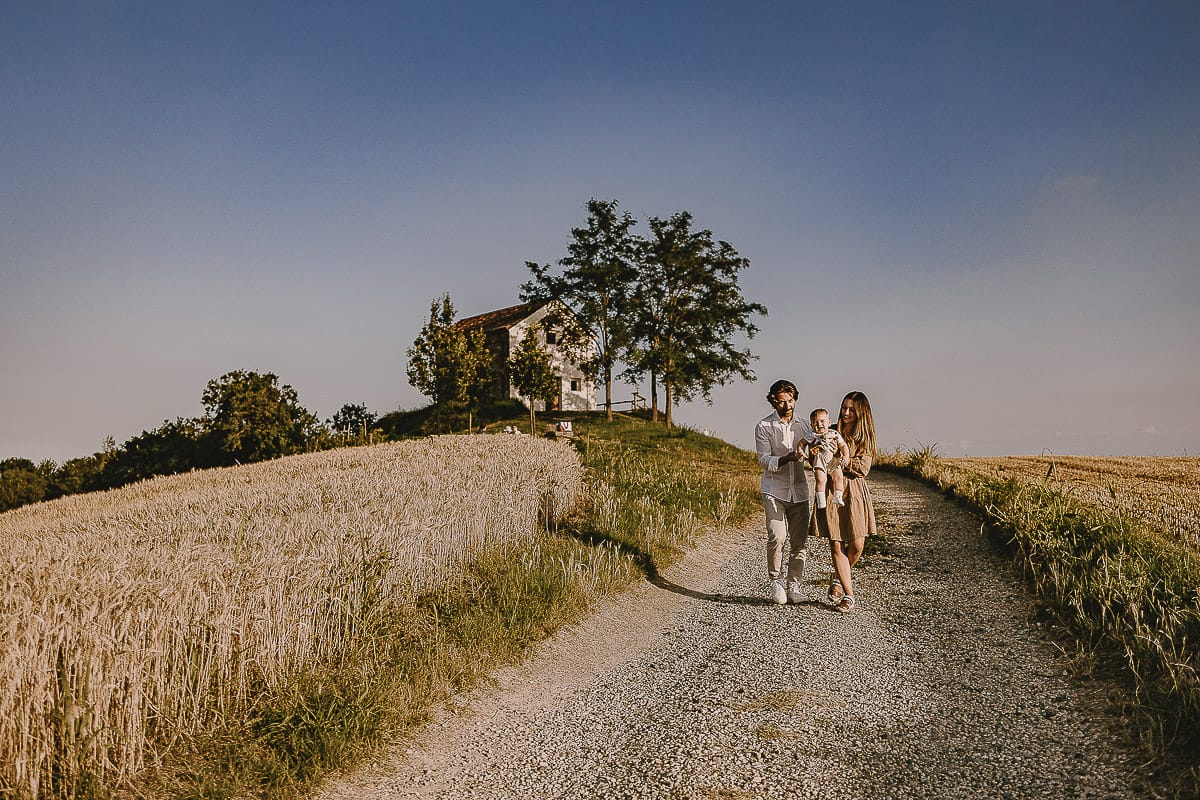 Servizio fotografico di famiglia a Torino: un tramonto dorato a Mombello di Torino. Chiara, Alessandro e il piccolo Leonardo camminano