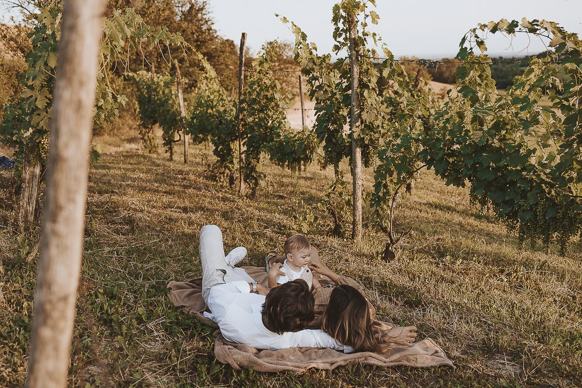 Servizio fotografico di famiglia a Torino: un tramonto dorato a Mombello di Torino. Chiara, Alessandro e il piccolo Leonardo sdraiati in un vigneto