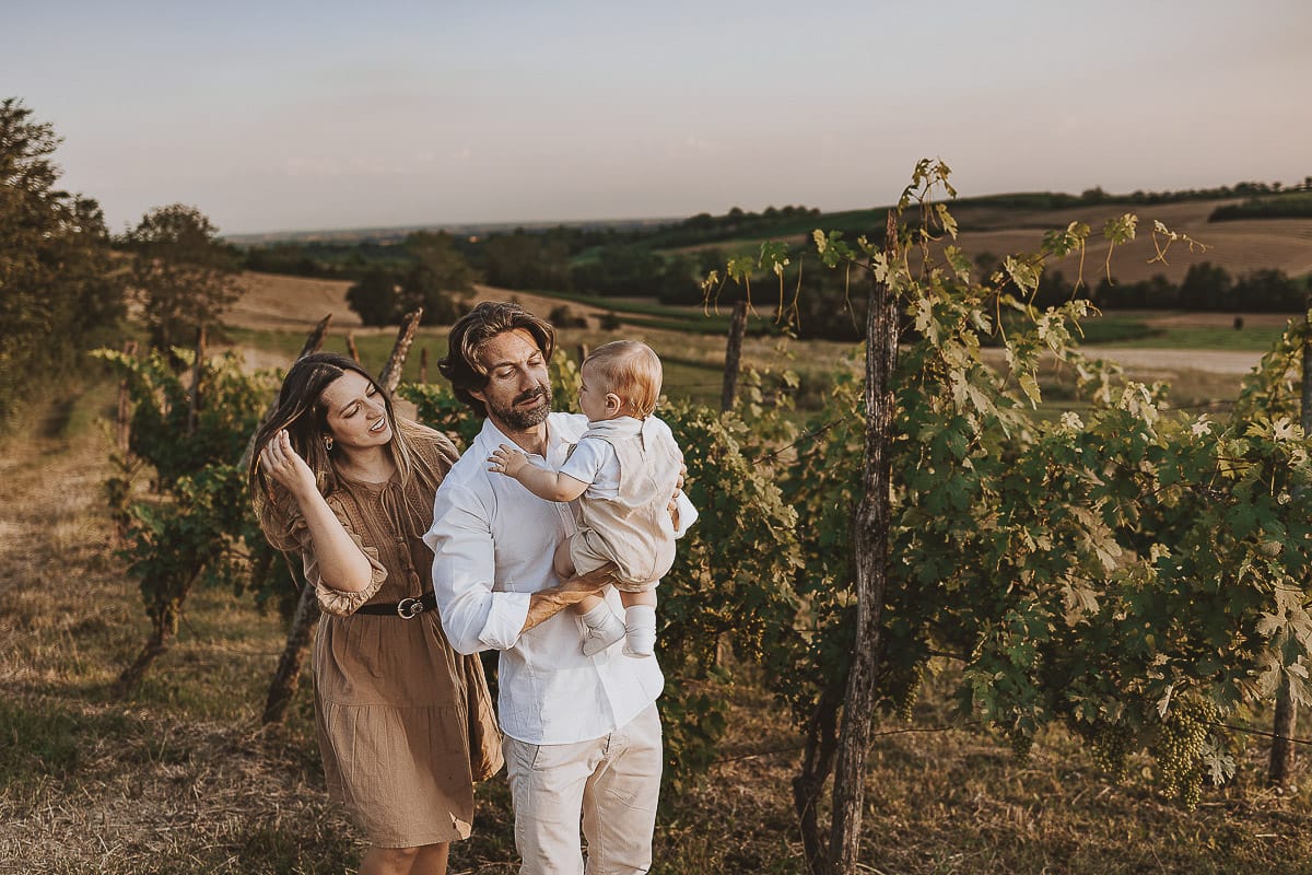 Servizio fotografico di famiglia a Torino: un tramonto dorato a Mombello di Torino. Chiara, Alessandro e il piccolo Leonardo camminano in un vigneto