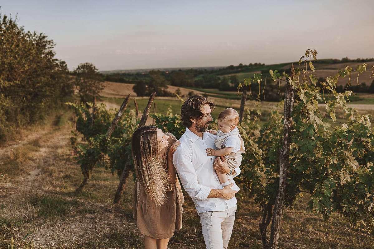 Servizio fotografico di famiglia a Torino: un tramonto dorato a Mombello di Torino. Chiara, Alessandro e il piccolo Leonardo camminano in un vigneto