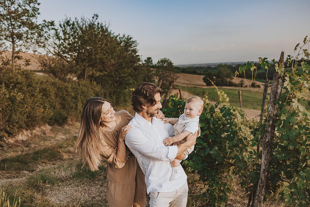 Servizio fotografico di famiglia a Torino: un tramonto dorato a Mombello di Torino. Chiara, Alessandro e il piccolo Leonardo camminano in un vigneto
