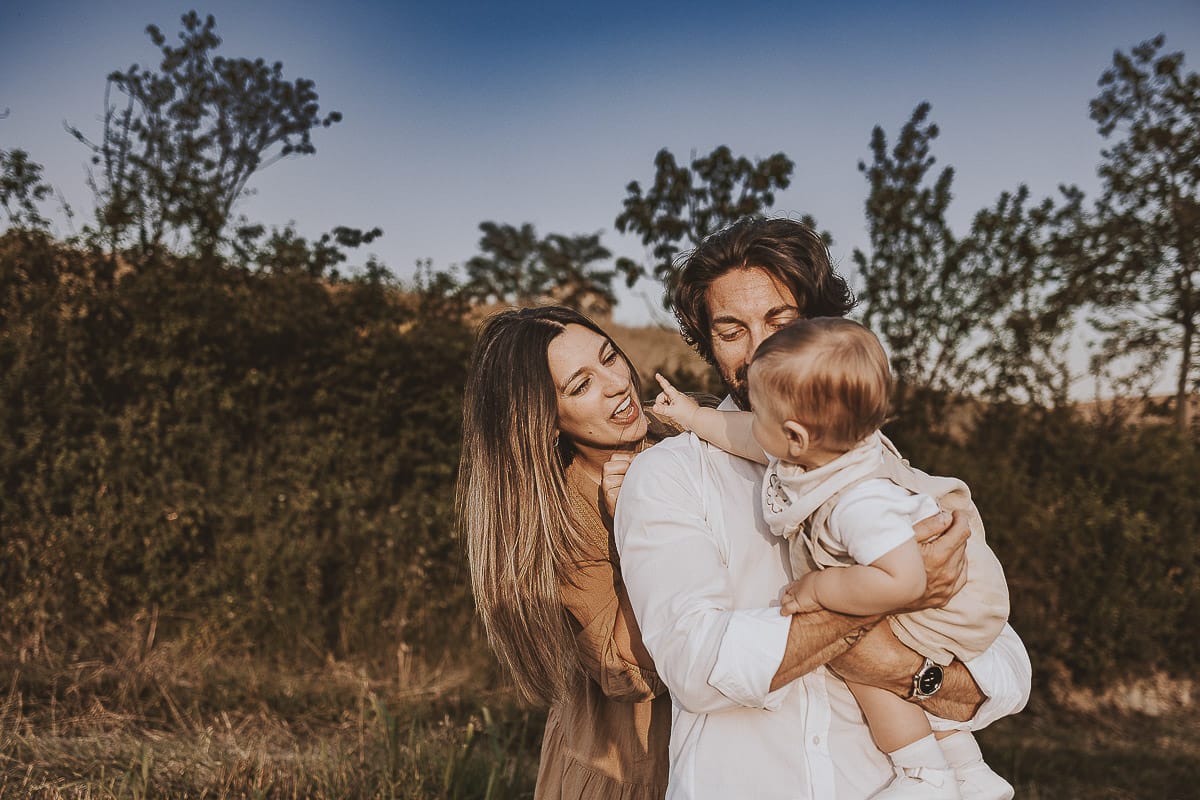 Servizio fotografico di famiglia a Torino: un tramonto dorato a Mombello di Torino. Chiara, Alessandro e il piccolo Leonardo camminano in un vigneto