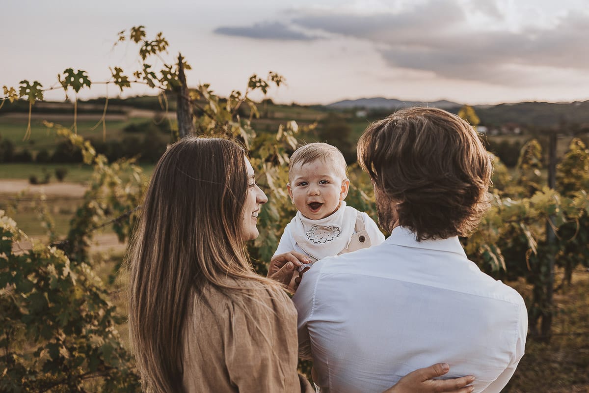 Servizio fotografico di famiglia a Torino: un tramonto dorato a Mombello di Torino. Chiara, Alessandro e il piccolo Leonardo camminano in un vigneto