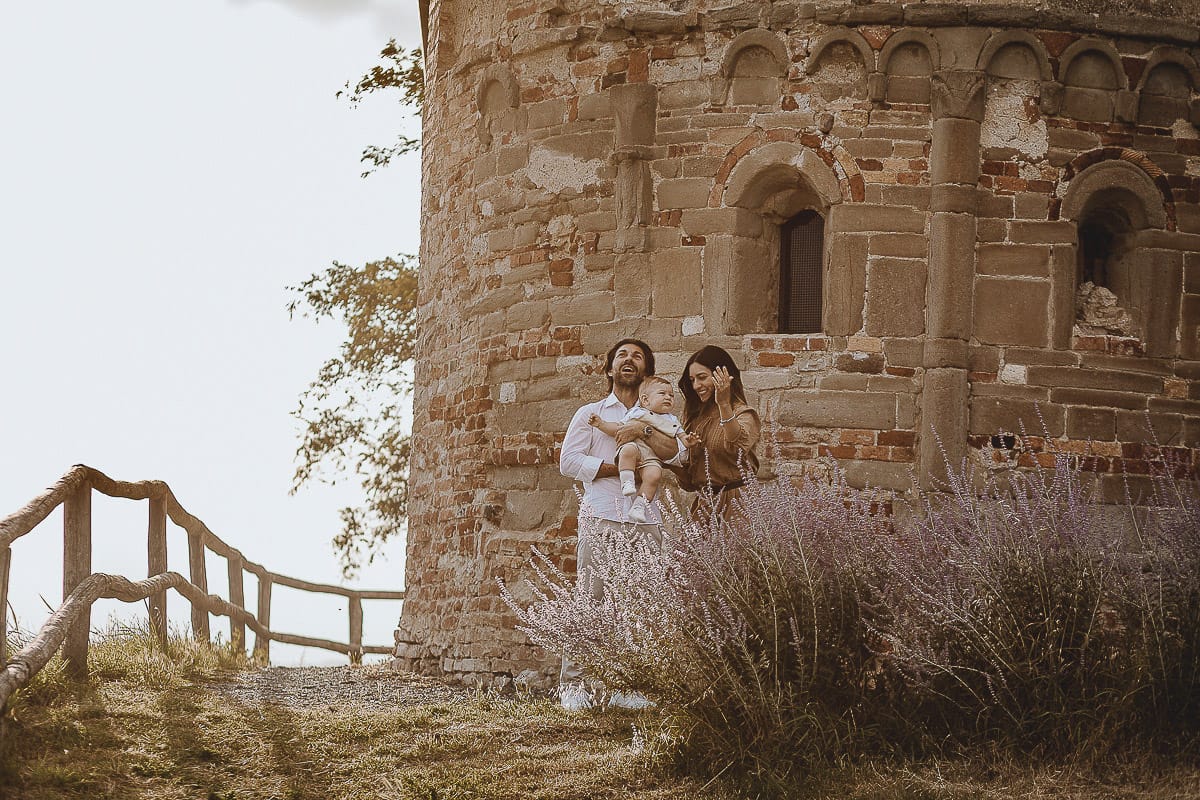 Servizio fotografico di famiglia a Torino: un tramonto dorato a Mombello di Torino. Chiara, Alessandro e leonardo in mezzo ad un cespuglio di fiori di colore lilla davanti alla chiesa romanica di San Lorenzo