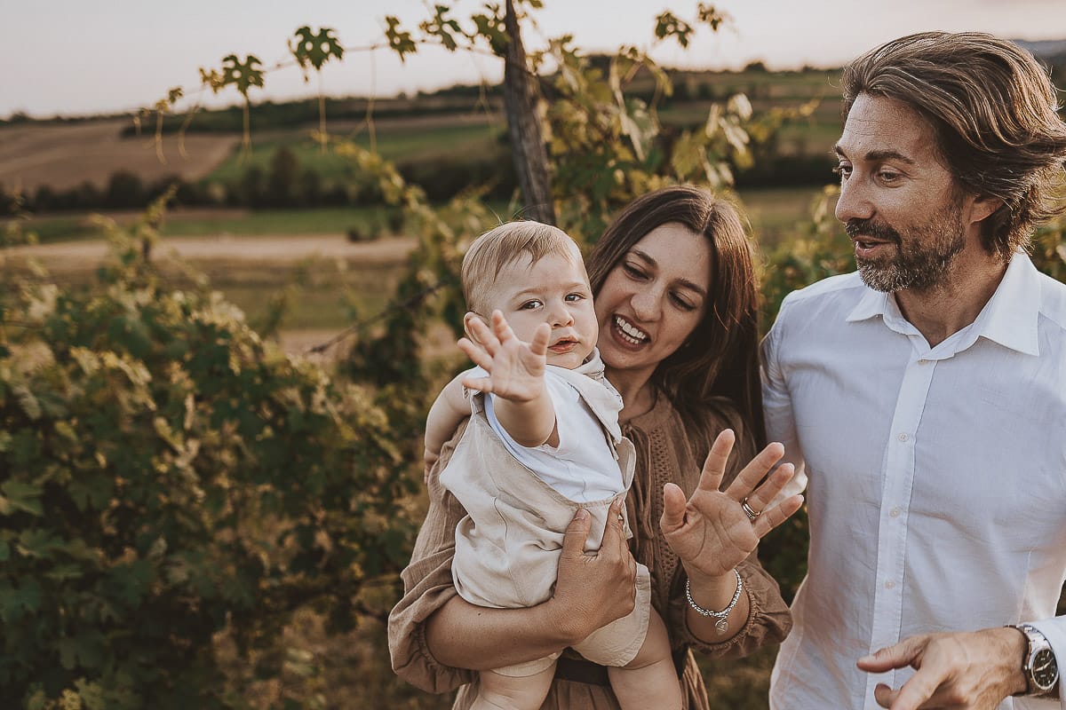 Servizio fotografico di famiglia a Torino: un tramonto dorato a Mombello di Torino. Chiara, Alessandro e il piccolo Leonardo camminano in un vigneto