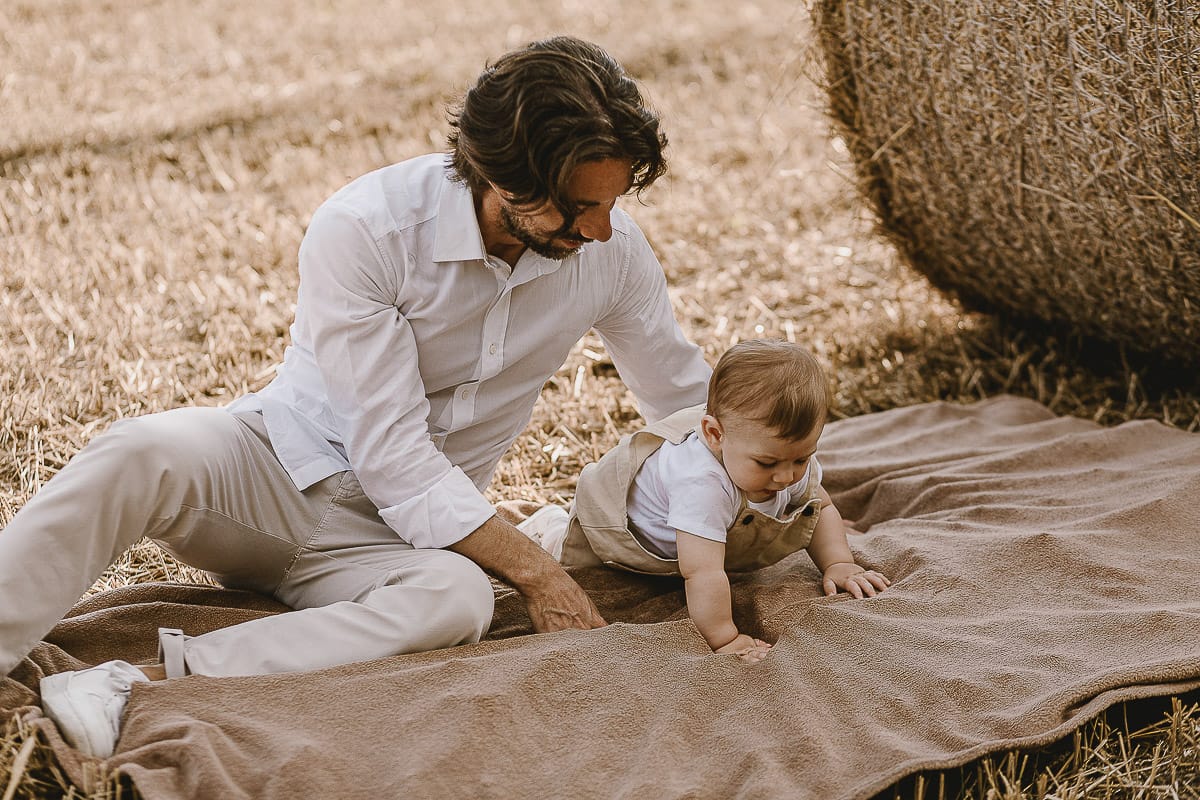 Servizio fotografico di famiglia a Torino: un tramonto dorato a Mombello di Torino. Alessandro e il piccolo Leonardo in un campo davanti ad una balla di fieno