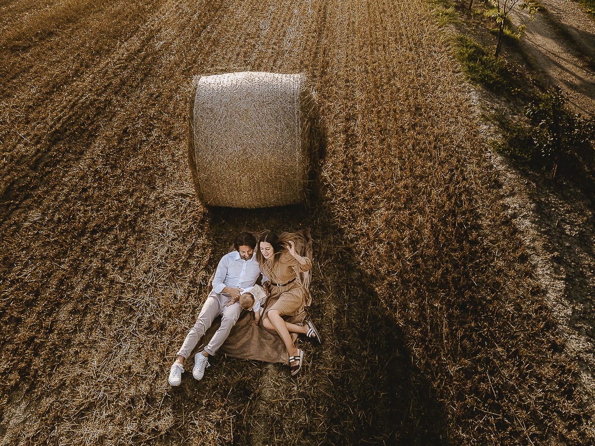 Servizio fotografico di famiglia a Torino: un tramonto dorato a Mombello di Torino. Chiara, Alessandro e il piccolo Leonardo distesi in un campo davanti ad una balla di fieno.