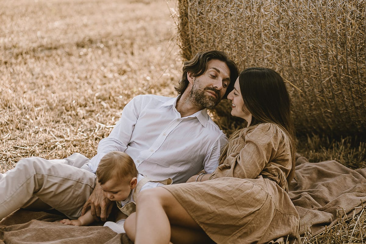 Servizio fotografico di famiglia a Torino: un tramonto dorato a Mombello di Torino. Chiara, Alessandro e il piccolo Leonardo distesi in un campo davanti ad una balla di fieno.