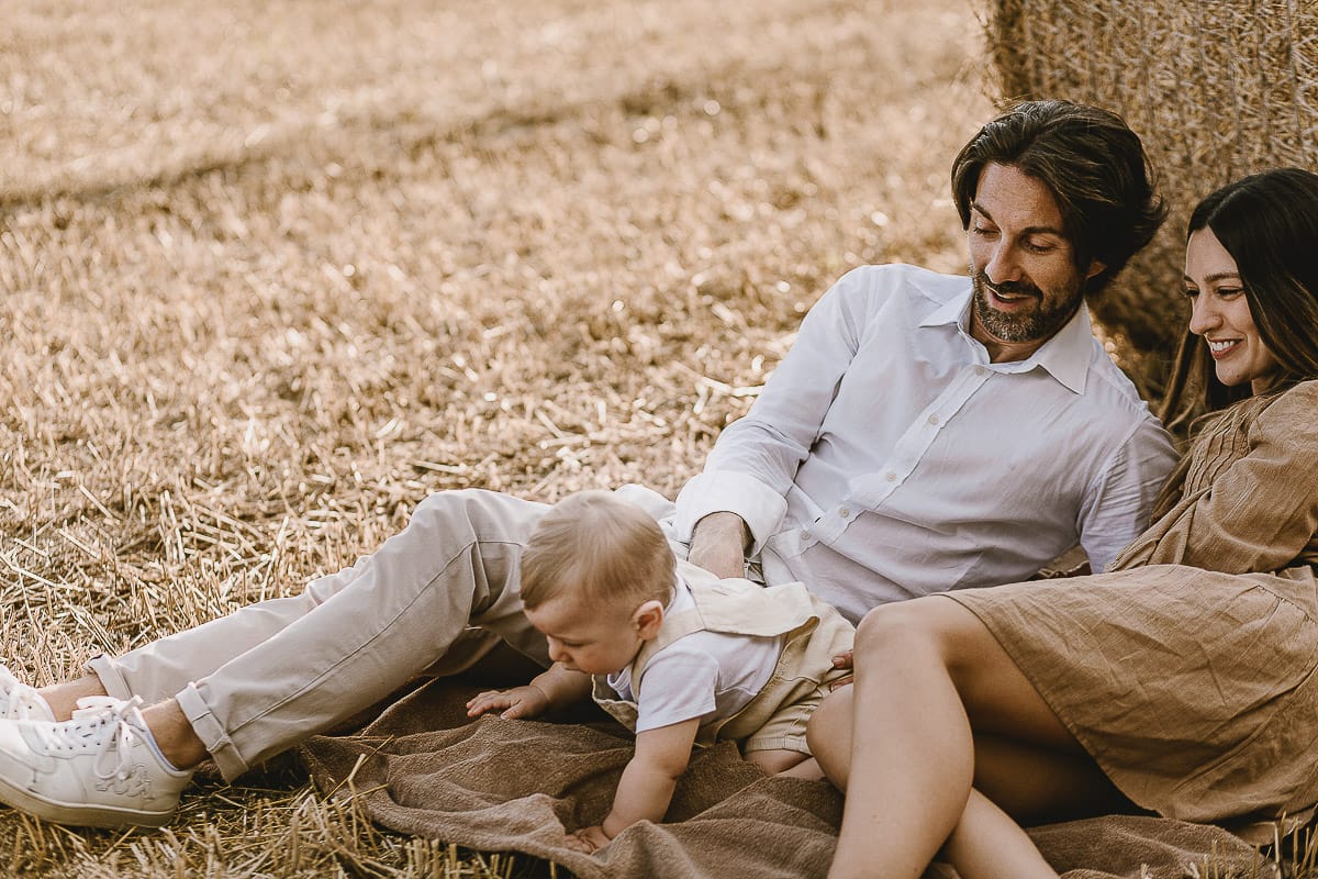 Servizio fotografico di famiglia a Torino: un tramonto dorato a Mombello di Torino. Chiara, Alessandro e il piccolo Leonardo distesi in un campo davanti ad una balla di fieno.