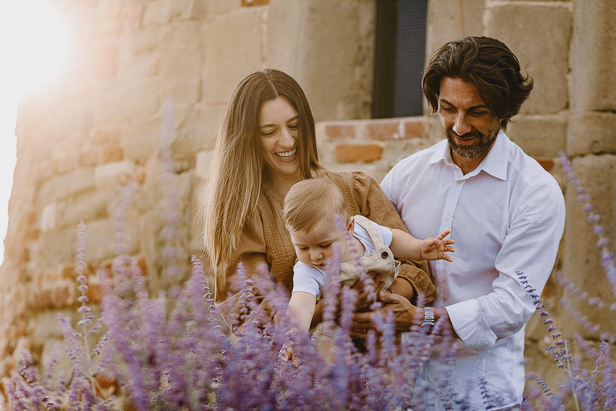 Servizio fotografico di famiglia a Torino: un tramonto dorato a Mombello di Torino. Chiara, Alessandro e leonardo in mezzo ad un cespuglio di fiori di colore lilla davanti alla chiesa romanica di San Lorenzo