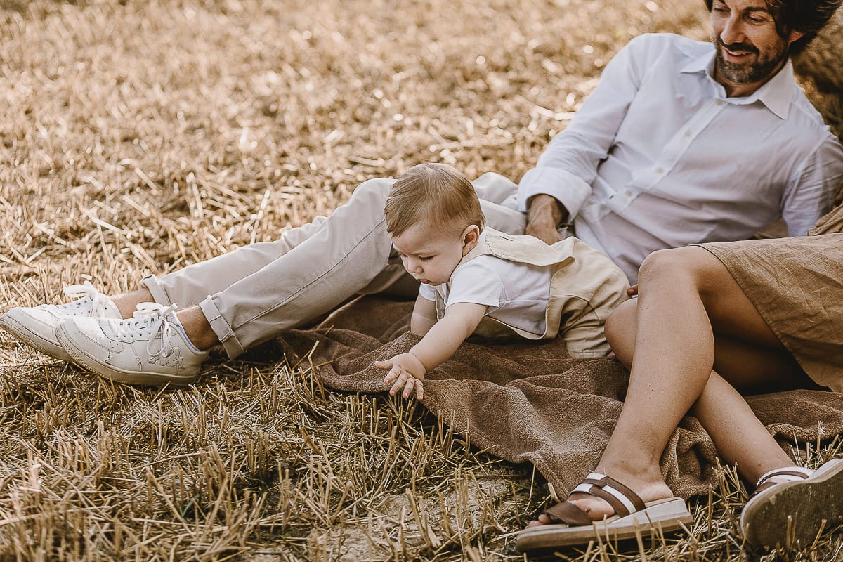 Servizio fotografico di famiglia a Torino: un tramonto dorato a Mombello di Torino. Chiara, Alessandro e il piccolo Leonardo distesi in un campo davanti ad una balla di fieno.